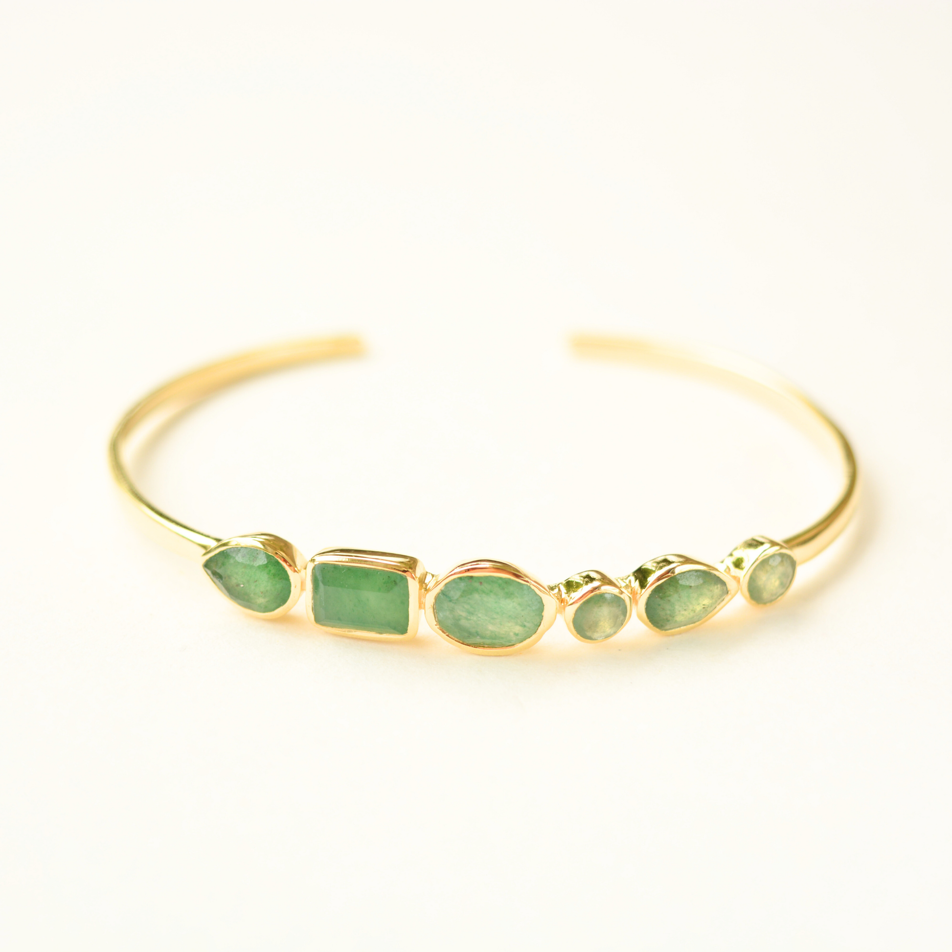 A gold-plated silver cuff bracelet featuring an assortment of green aventurine stones in varying shapes, centered against a plain white background.
