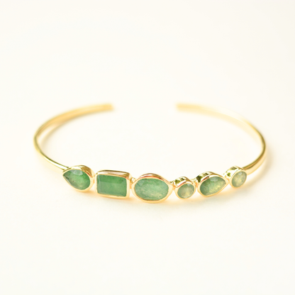 A gold-plated silver cuff bracelet featuring an assortment of green aventurine stones in varying shapes, centered against a plain white background.