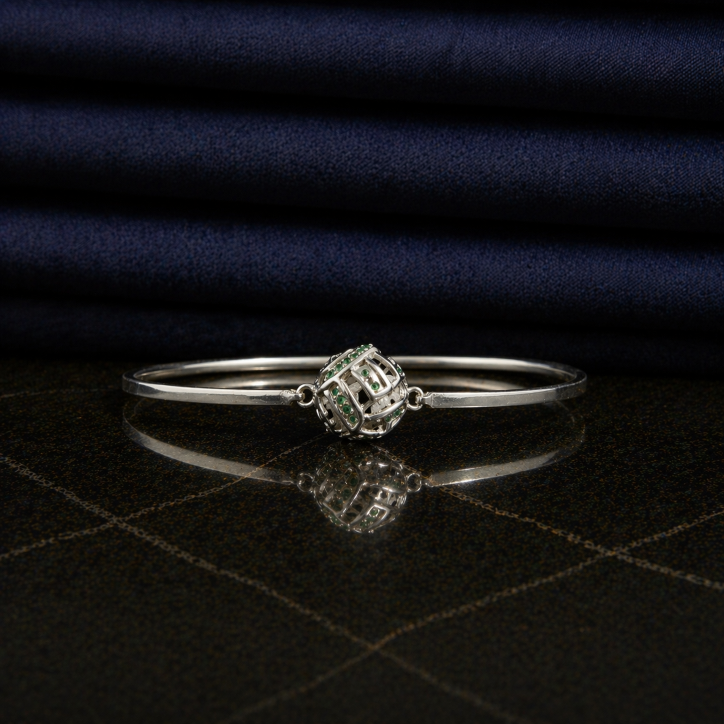 Front view of the Green Glow Rolling Bangle on a dark reflective surface, highlighting the vibrant green CZ stone accents and sleek minimal frame.