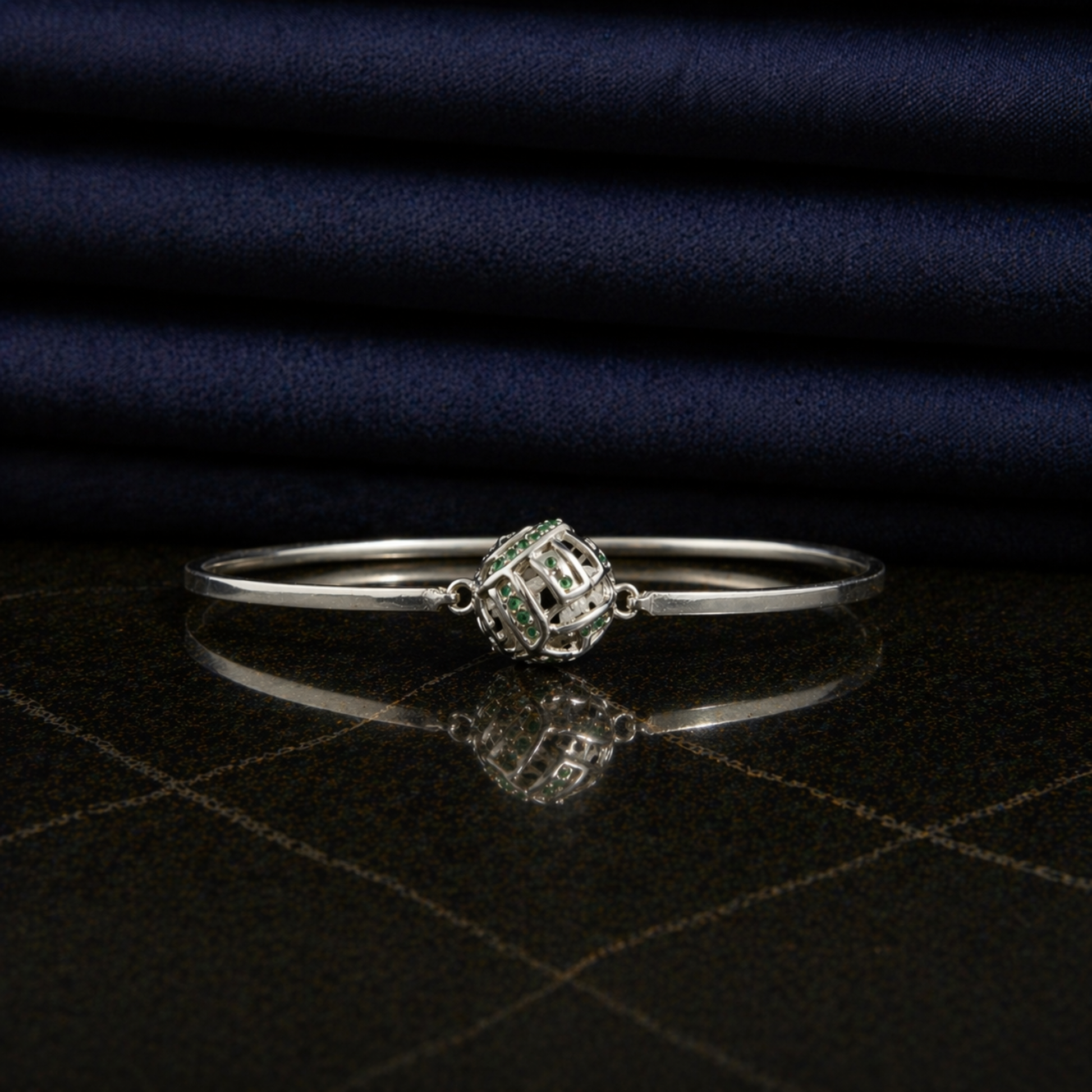 Front view of the Green Glow Rolling Bangle on a dark reflective surface, highlighting the vibrant green CZ stone accents and sleek minimal frame.