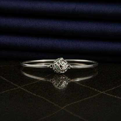 Front view of the Green Glow Rolling Bangle on a dark reflective surface, highlighting the vibrant green CZ stone accents and sleek minimal frame.