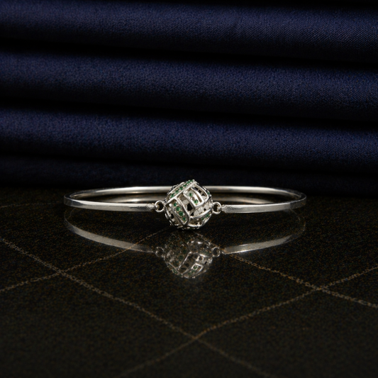 Front view of the Green Glow Rolling Bangle on a dark reflective surface, highlighting the vibrant green CZ stone accents and sleek minimal frame.