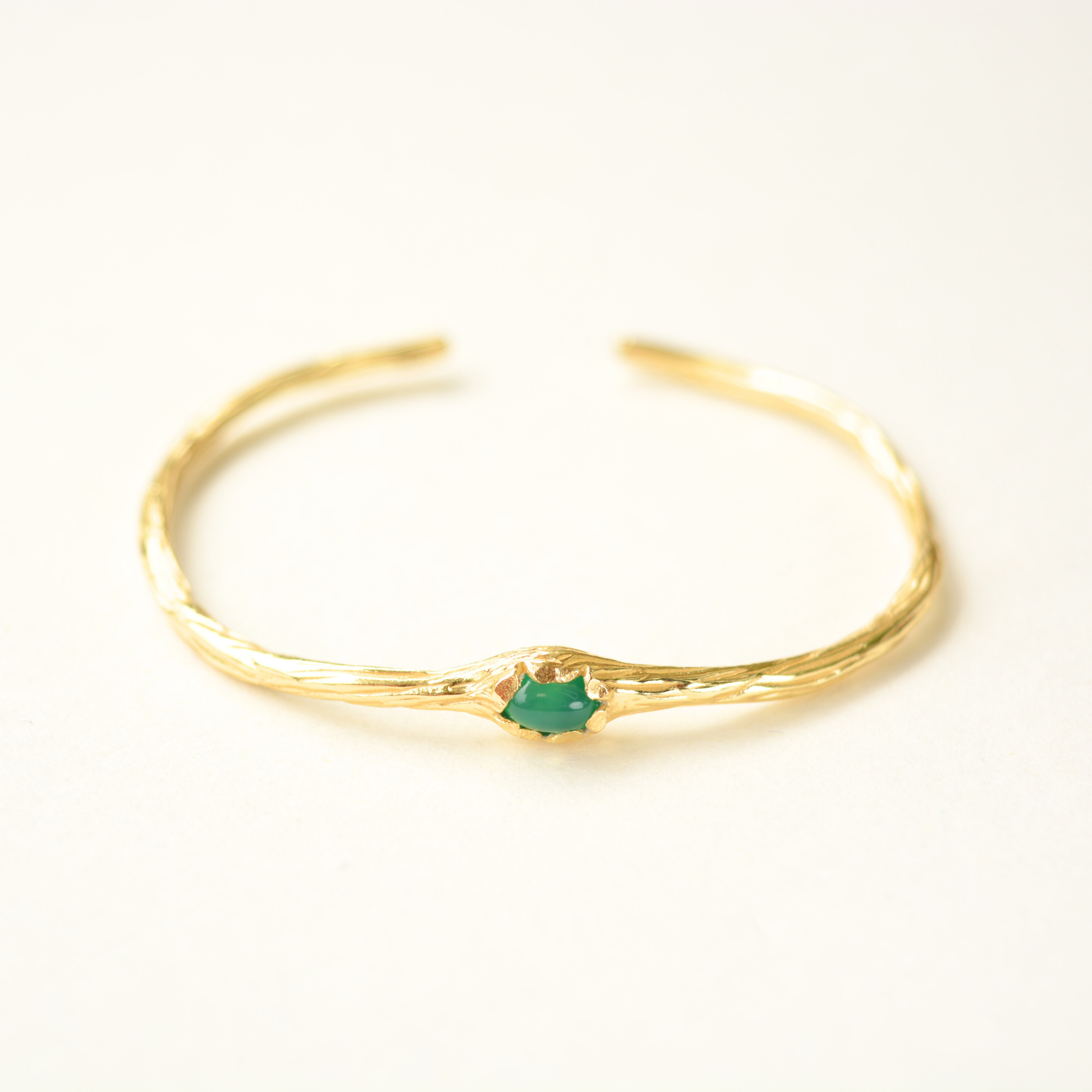 Gold-plated open cuff bracelet with a small, oval green onyx stone and textured metal finish.