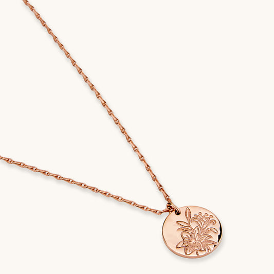 A close-up studio shot of a rose gold-toned medallion pendant with detailed embossed botanical artwork, highlighting its refined and classic design.