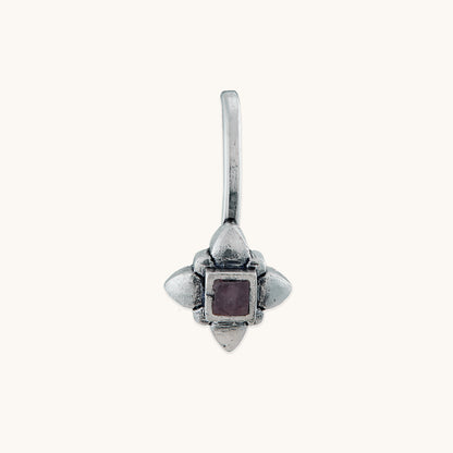 Front-facing view of a handcrafted silver nose clip, showcasing a symmetrical floral-inspired frame holding a deep purple stone.