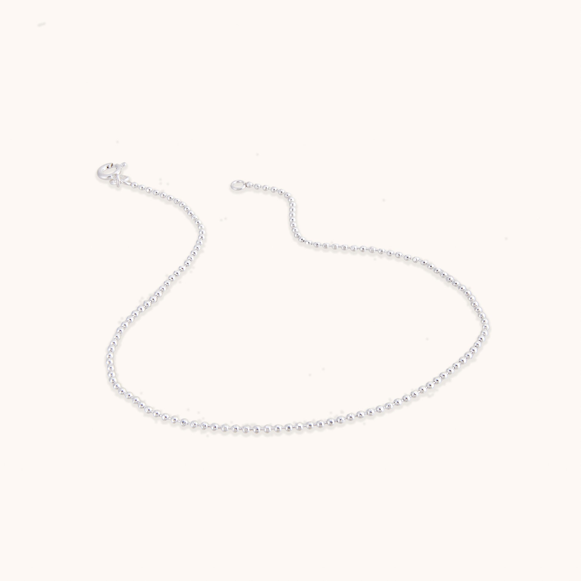 A delicate, minimalist silver chain featuring evenly spaced small beads along the strand, shown with a secure clasp.
