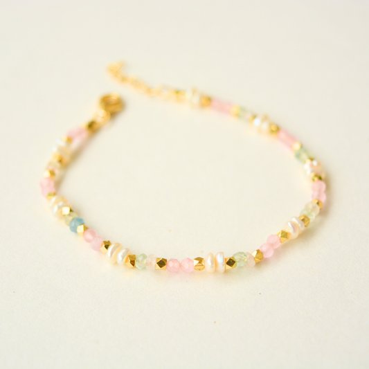 A gold-plated silver beaded bracelet featuring a delicate arrangement of soft pink, green, and white pearls with small metallic gold spacers, on a white background.