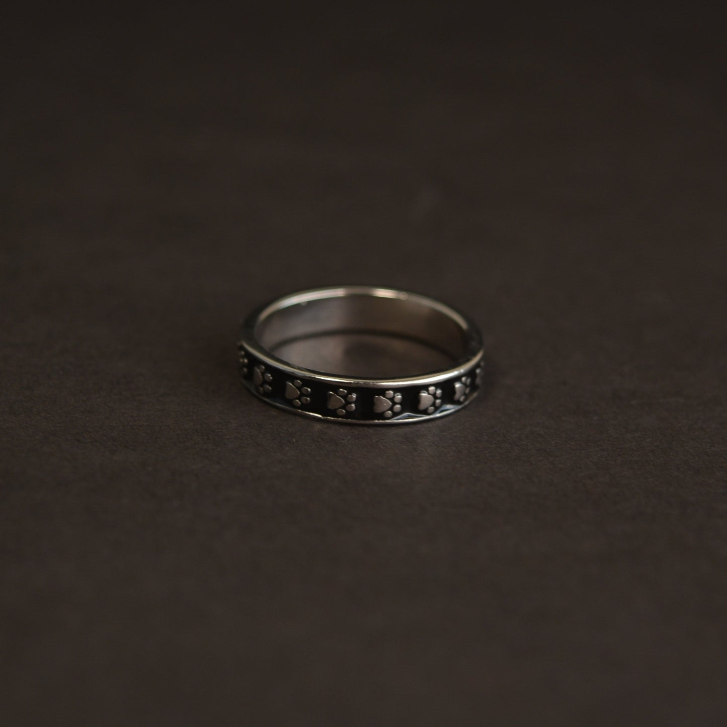 A minimalist 925 sterling silver ring featuring a delicate black enamel animal paw print motif, isolated on a black background.
