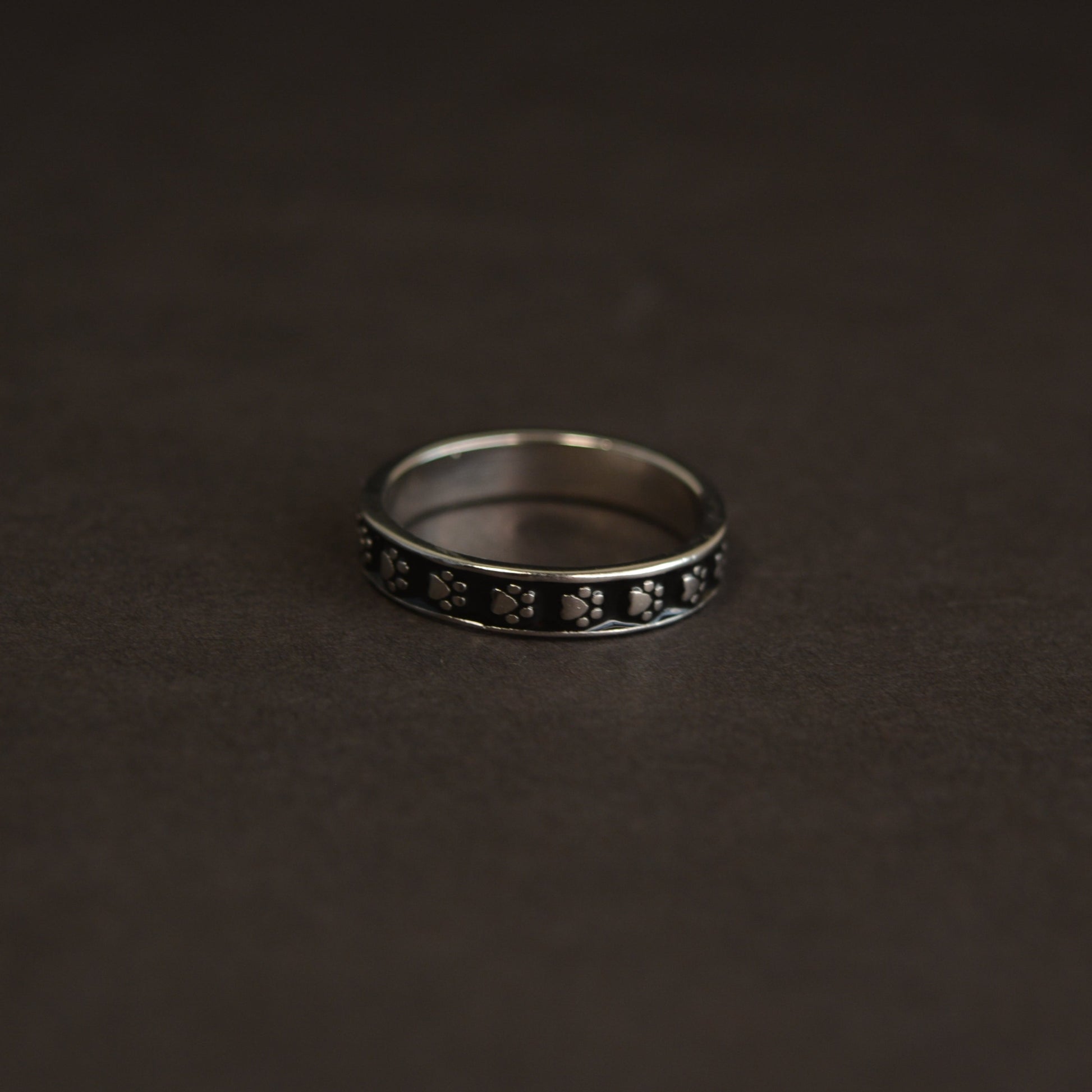 A minimalist 925 sterling silver ring featuring a delicate black enamel animal paw print motif, isolated on a black background.