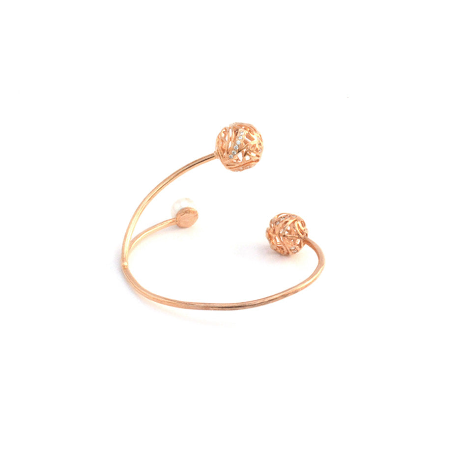 A rose gold open-style bracelet designed with two decorative, hollow spherical charms and a single pearl, isolated on a white background.