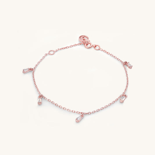 A delicate rose gold chain bracelet with dangling, baguette-cut stone charms, shown isolated against a clean, white background.