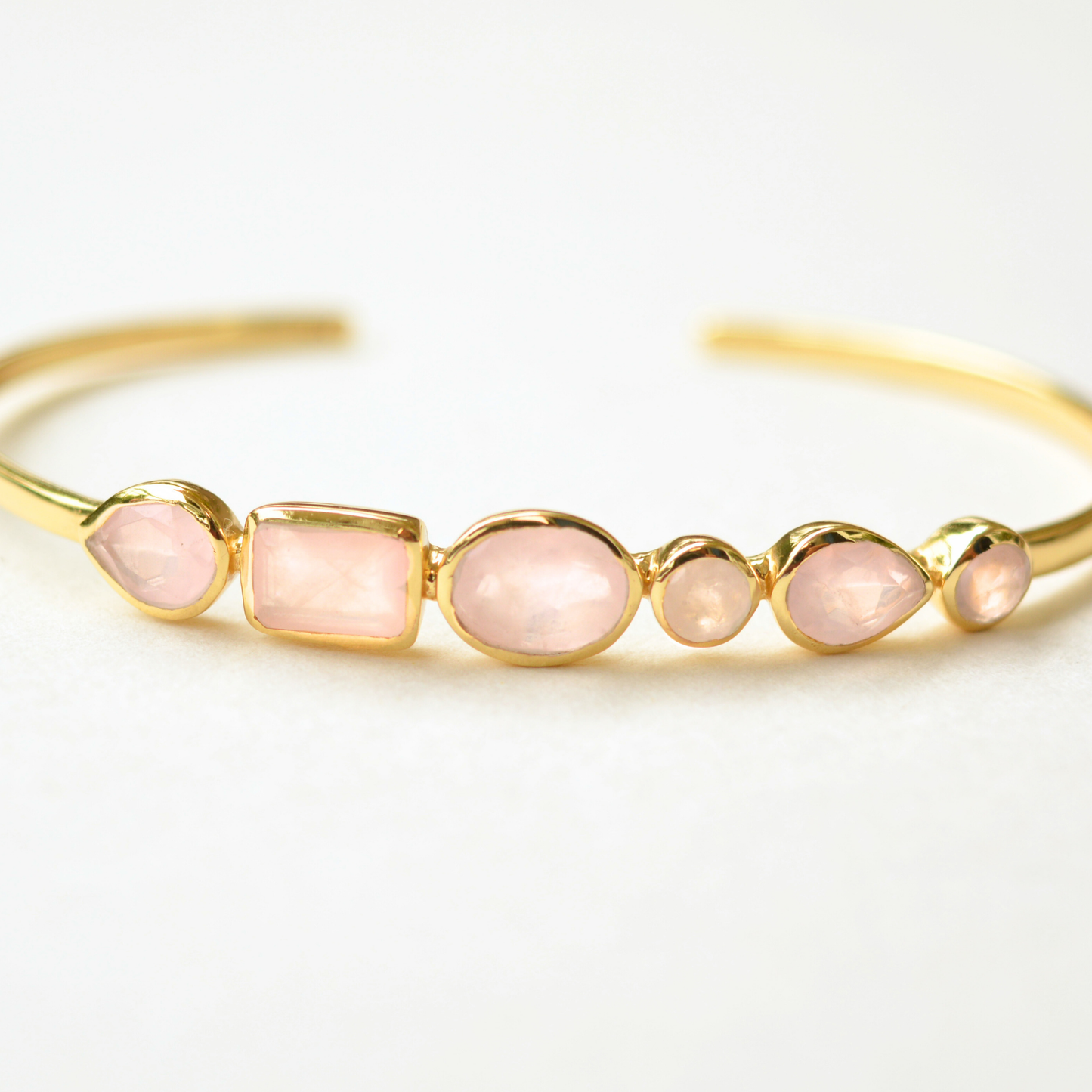 Gold-plated cuff bracelet featuring a row of assorted rose quartz stones in various cuts.