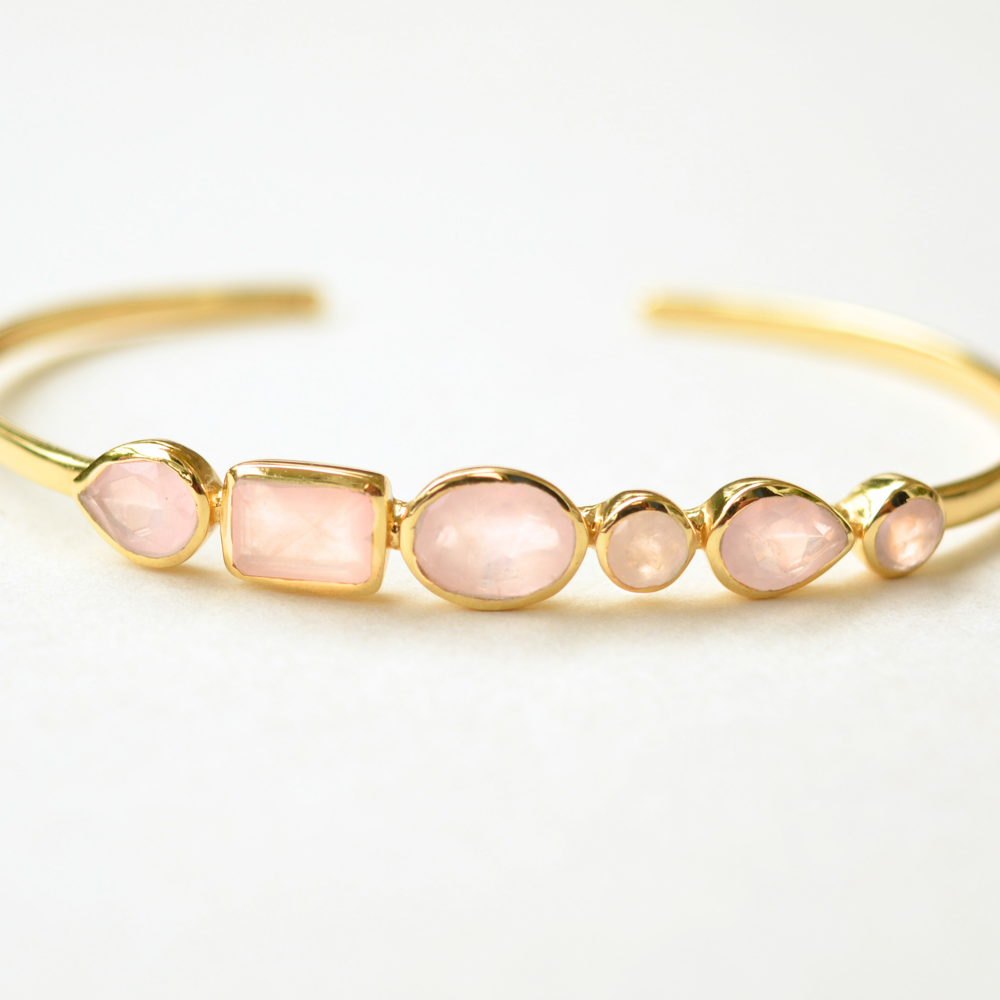 Gold-plated cuff bracelet featuring a row of assorted rose quartz stones in various cuts.