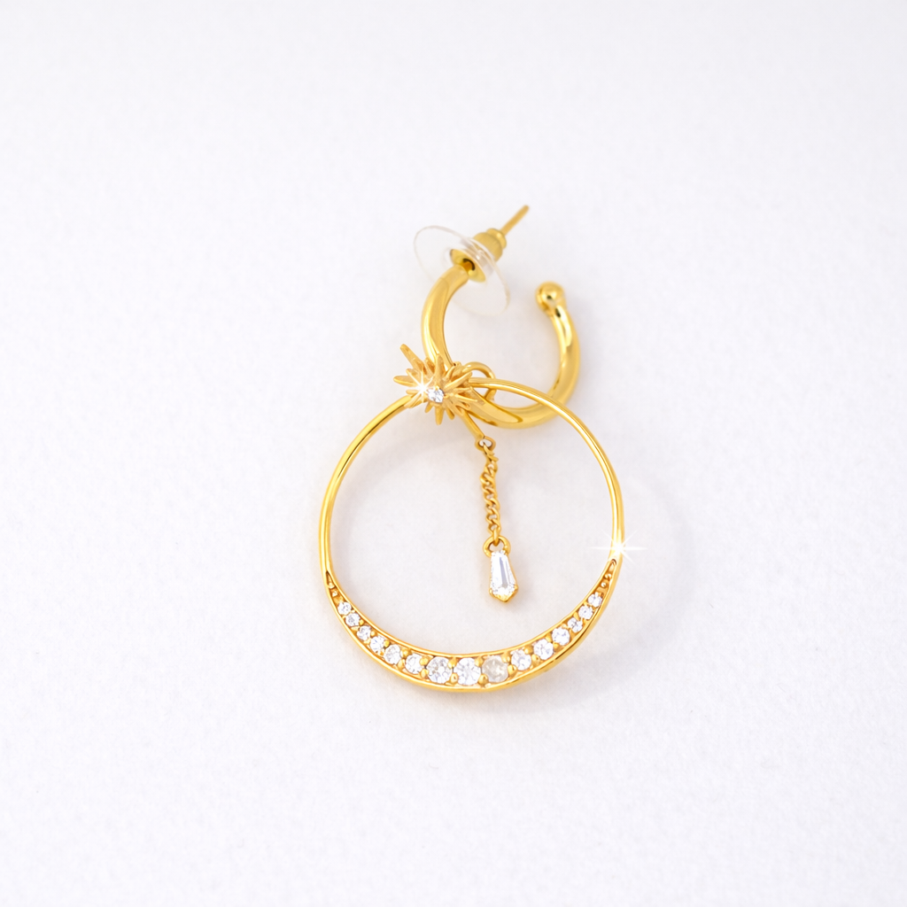 Elegant layered gold hoop earring combining a crescent crystal-studded band with a delicate celestial sunburst charm and a dangling baguette-cut gemstone.