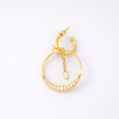 Elegant layered gold hoop earring combining a crescent crystal-studded band with a delicate celestial sunburst charm and a dangling baguette-cut gemstone.