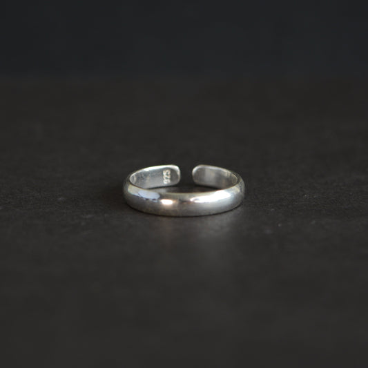 Eye-level shot of a minimalist 925 sterling silver band ring with an adjustable open back, displayed on a dark textured surface.