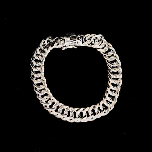 A high-shine silver curb link bracelet for men featuring a thick, interlocking chain design and a detailed decorative clasp, isolated on a black background.