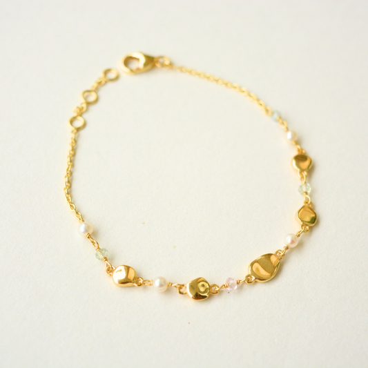 Gold-finished silver chain bracelet with organic pebble-shaped charms, small white pearls, and accent gemstones.