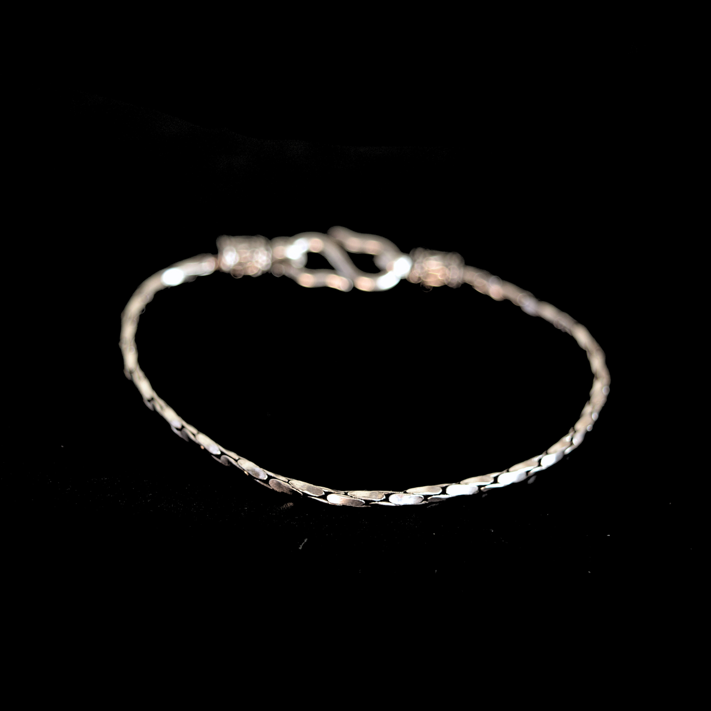 Angled view of a textured silver chain bracelet on a solid black background.