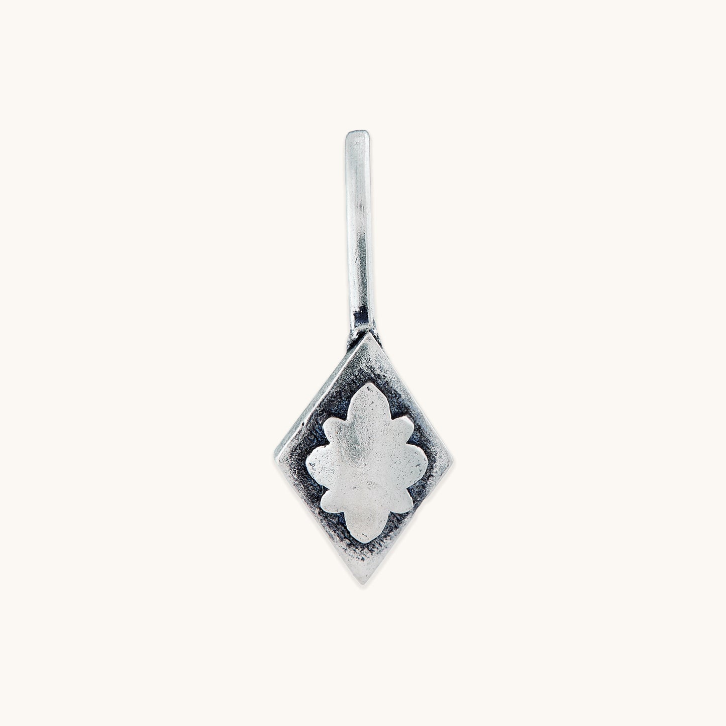 A close-up, front-facing studio shot of a diamond-shaped silver clip-on featuring a raised, central floral embossed design on a clean, light-colored background.