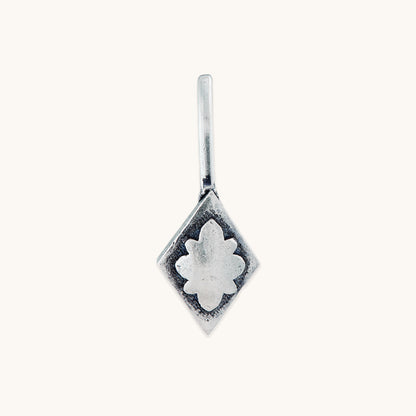 A close-up, front-facing studio shot of a diamond-shaped silver clip-on featuring a raised, central floral embossed design on a clean, light-colored background.