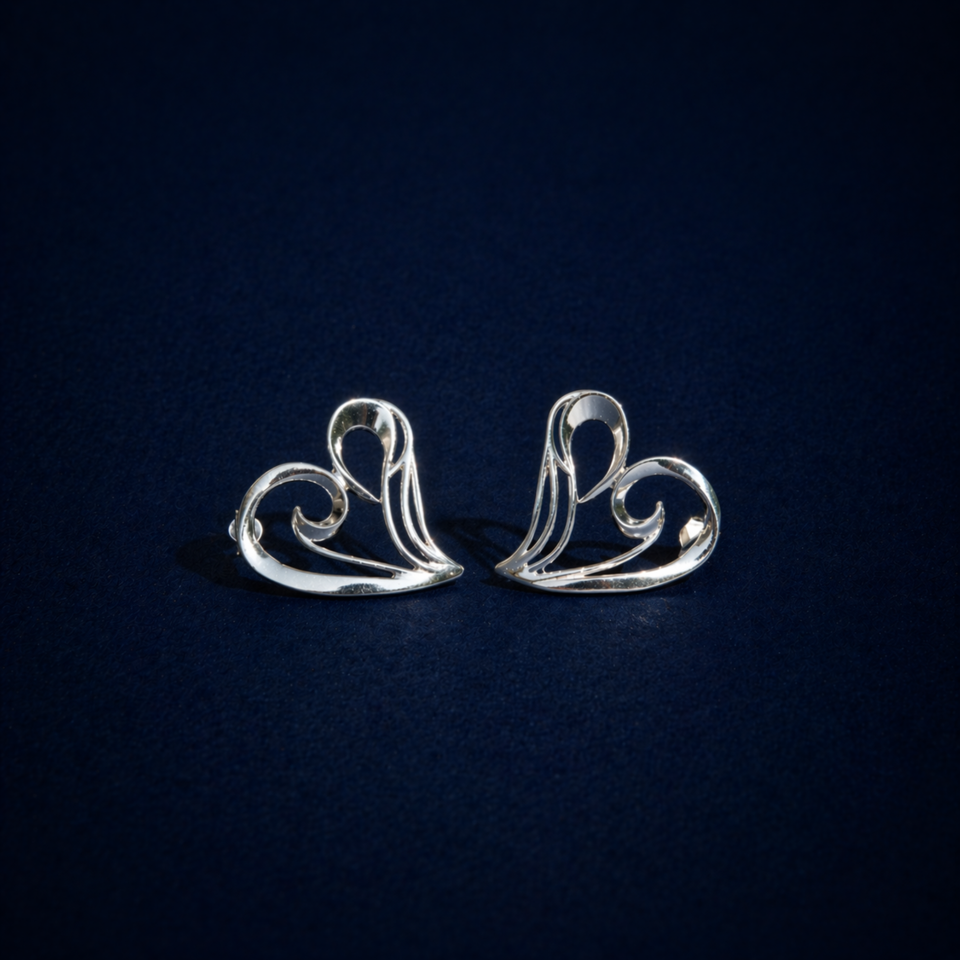 Studio flat lay of the Trueform Heart in Studs on a deep blue background, showcasing the lightweight and modern romantic jewelry design.