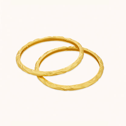 Two brass bangles in gold plating, featuring a continuous flowing design on a white background
