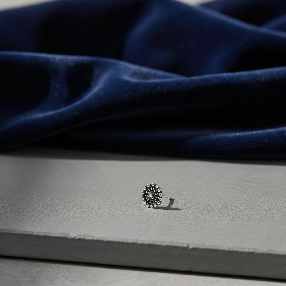 Radiant Nose Pin in oxidised 925 sterling silver with a circular floral design, displayed on a neutral surface with a soft blue fabric background.