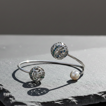 Silver Rolling Cuff Bracelet with open spherical ends and pearl accent, displayed on a textured stone surface in natural light.