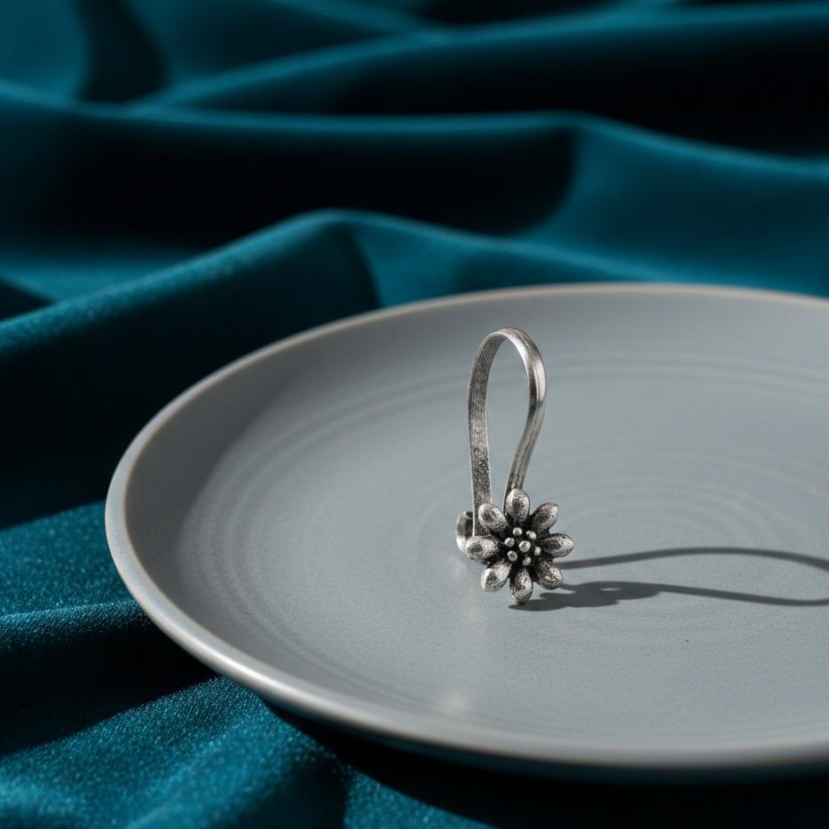 Silver blossom nose clip with a delicate floral design placed on a ceramic plate against a teal fabric background in soft natural light