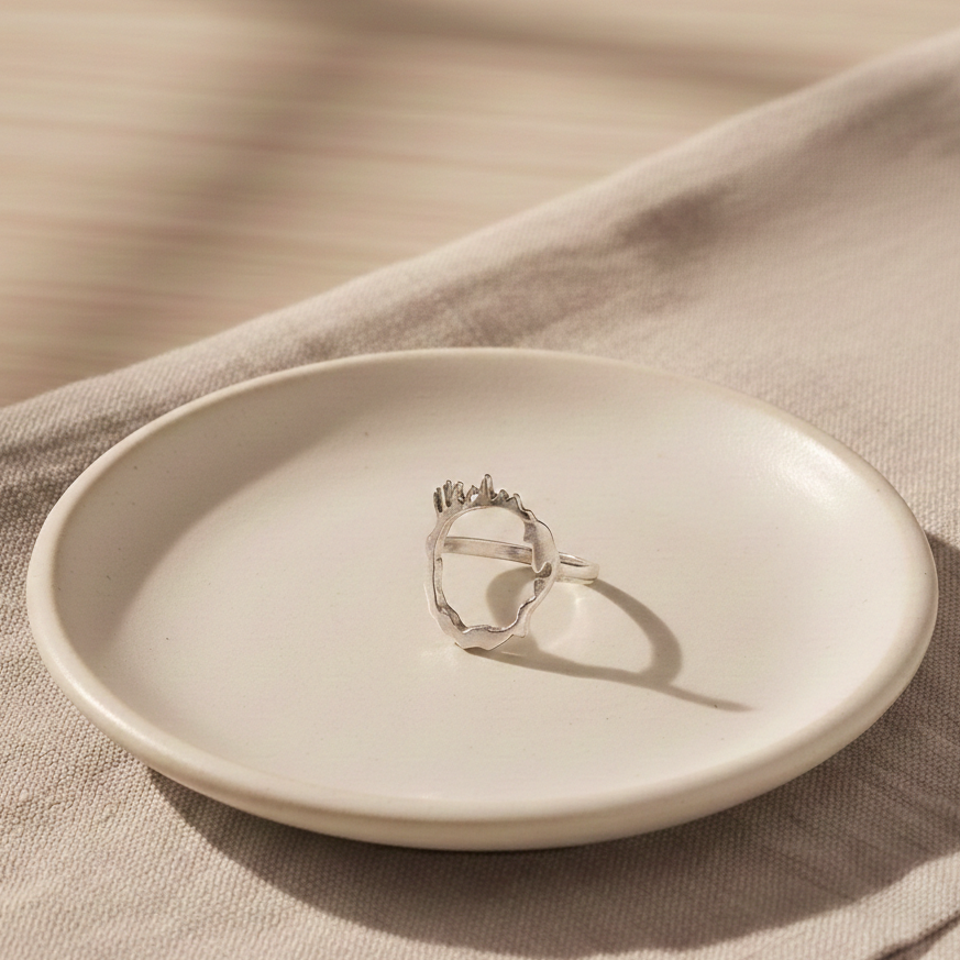 Contemporary silver drip ring showcased on ceramic dish with soft textiles.