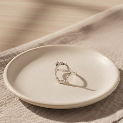 Contemporary silver drip ring showcased on ceramic dish with soft textiles.