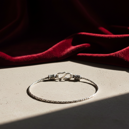 Unisex silver snake bracelet in 925 sterling silver featuring a sleek textured chain and hook clasp, styled on a stone surface with a rich red fabric backdrop.