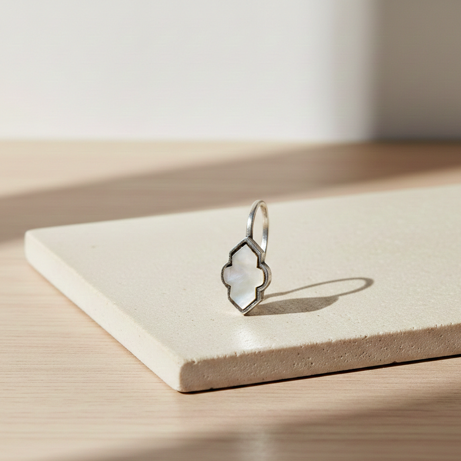 Close-up of a silver clip-on earring featuring a geometric iridescent inlay detail displayed on a minimalist pedestal in soft natural light.

