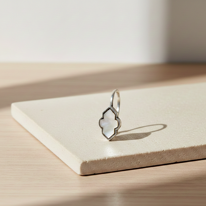 Close-up of a silver clip-on earring featuring a geometric iridescent inlay detail displayed on a minimalist pedestal in soft natural light.
