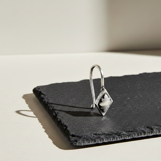 Sunbeam Silver Clip-On nose jewelry featuring a square frame with a delicate leaf motif, displayed on a textured black slate tile in warm natural light.