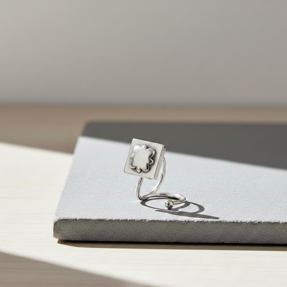 Sterling silver nose pin featuring a square floral sunburst design on a sleek curved post, displayed on a minimalist stone surface in soft natural light.