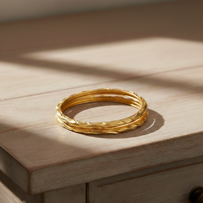 Set of textured gold infinity bangles stacked together on a wooden surface in warm natural light.