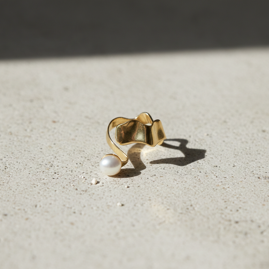 Gold Wavy Climber Ring featuring a sculpted wave design with a single pearl accent, displayed on a textured neutral surface in natural light.