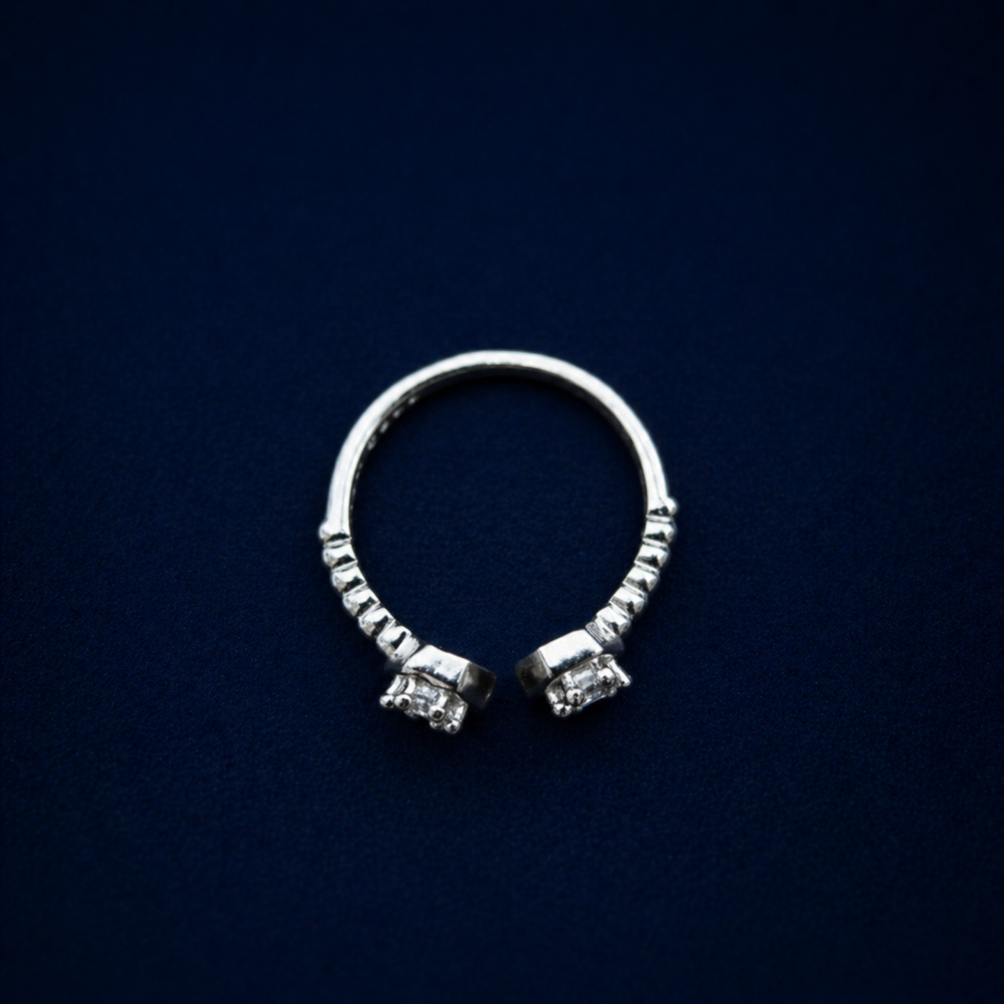 A top-down view of the handcrafted A Little Spark Ring on a dark navy background, highlighting the open adjustable band and the dual hexagonal cubic zirconia settings.