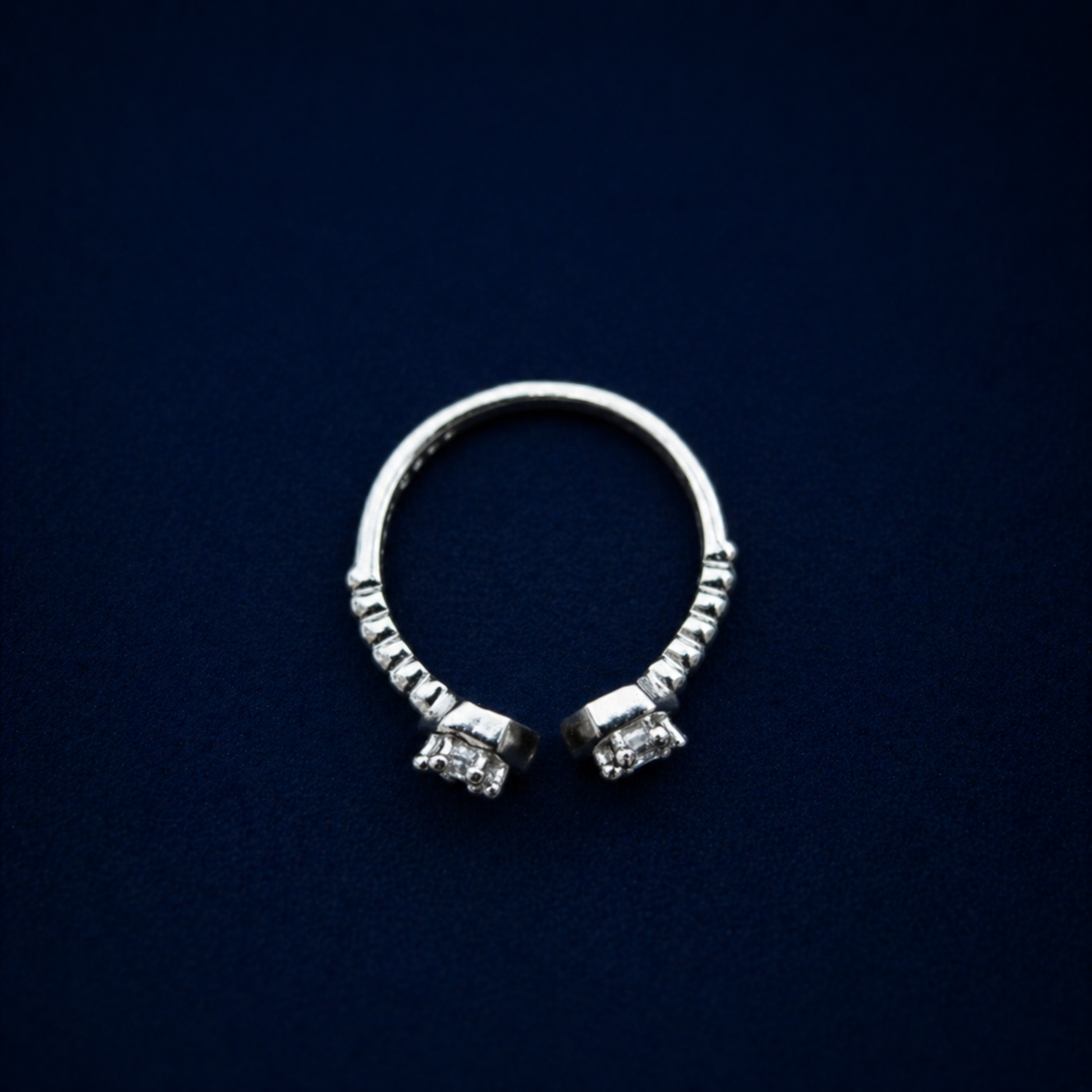 A top-down view of the handcrafted A Little Spark Ring on a dark navy background, highlighting the open adjustable band and the dual hexagonal cubic zirconia settings.