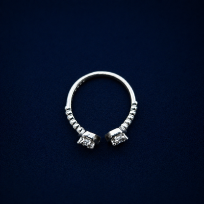 A top-down view of the handcrafted A Little Spark Ring on a dark navy background, highlighting the open adjustable band and the dual hexagonal cubic zirconia settings.