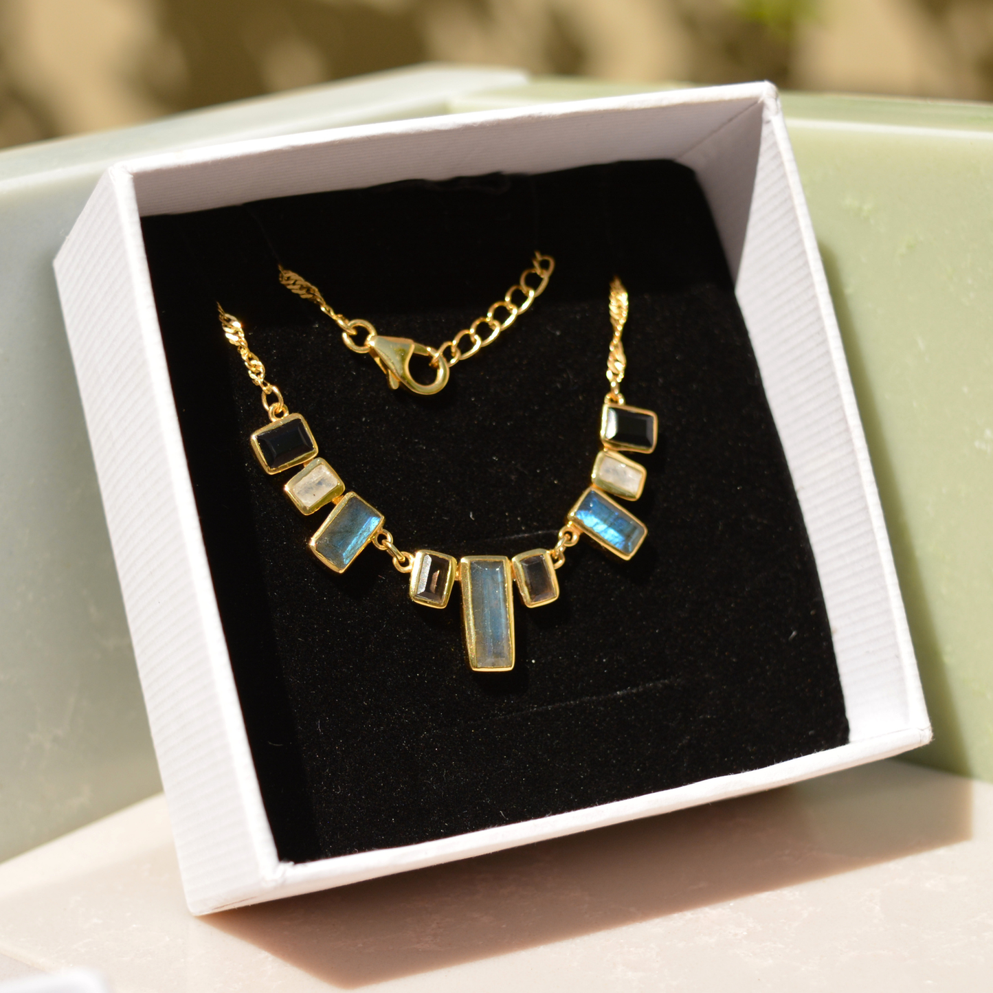 A handcrafted 18kt gold plated A Story of Stones necklace featuring natural labradorite, moonstone, and black onyx rectangular links, presented in a luxury white MAREECI gift box.