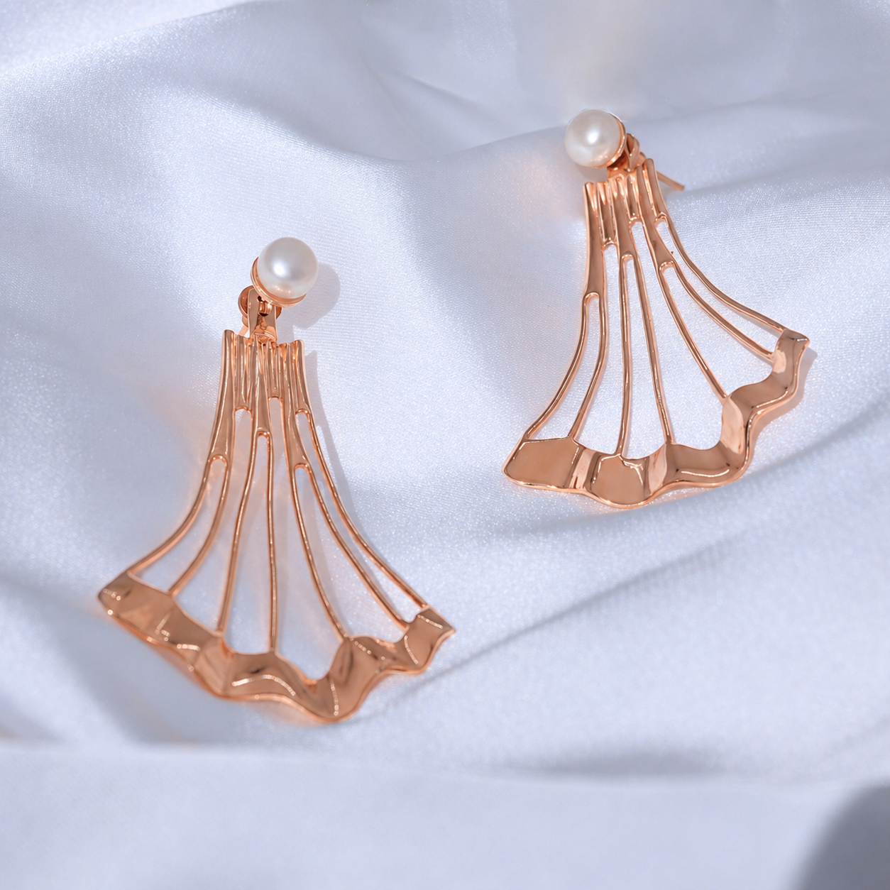 A close-up view of the Blush Tide earrings on white silk fabric, highlighting the flowing rose gold plated duster design and the lustrous real freshwater pearl studs.