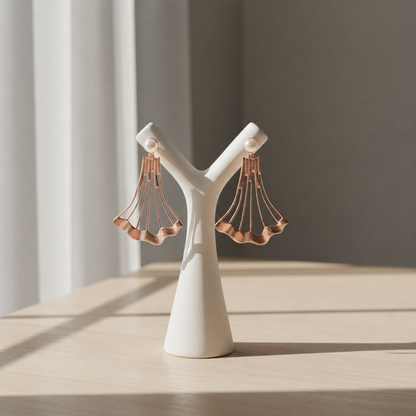 Handcrafted Blush Tide shoulder duster earrings in rose gold plated brass displayed on a minimal white sculptural stand, featuring a fan-shaped architectural design topped with real freshwater pearls.