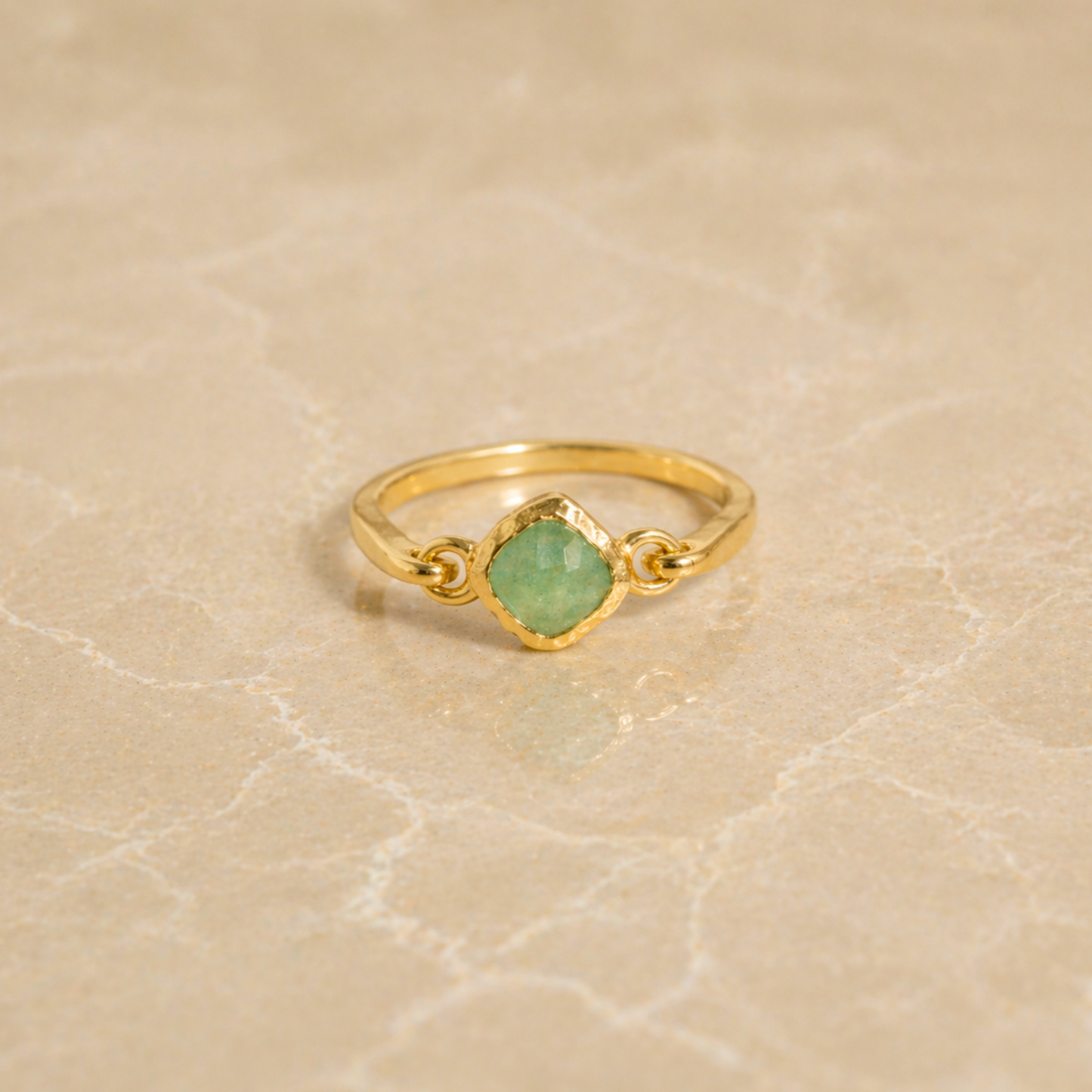 Frontal view of the Calm Aura Ring on a neutral textured surface, showcasing the modern minimal design and the calming glow of the green aventurine stone.