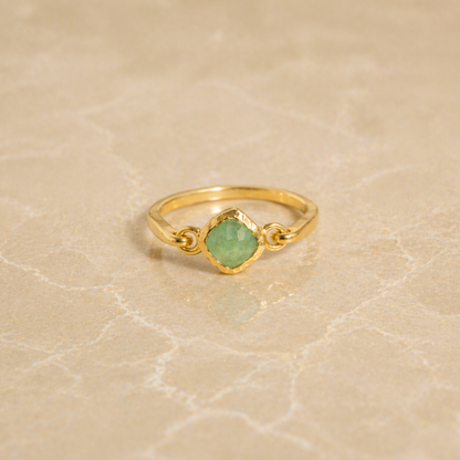 Frontal view of the Calm Aura Ring on a neutral textured surface, showcasing the modern minimal design and the calming glow of the green aventurine stone.