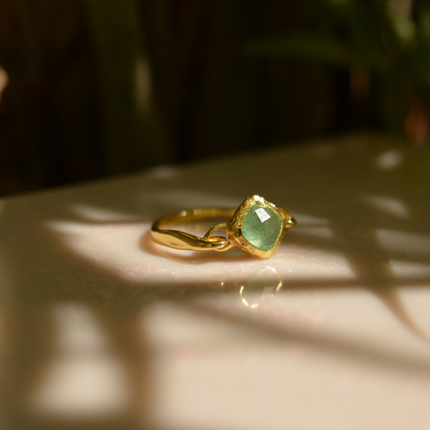 A handcrafted 18kt gold plated Calm Aura Ring featuring a square green aventurine stone, captured in warm natural sunlight with soft leaf shadows.