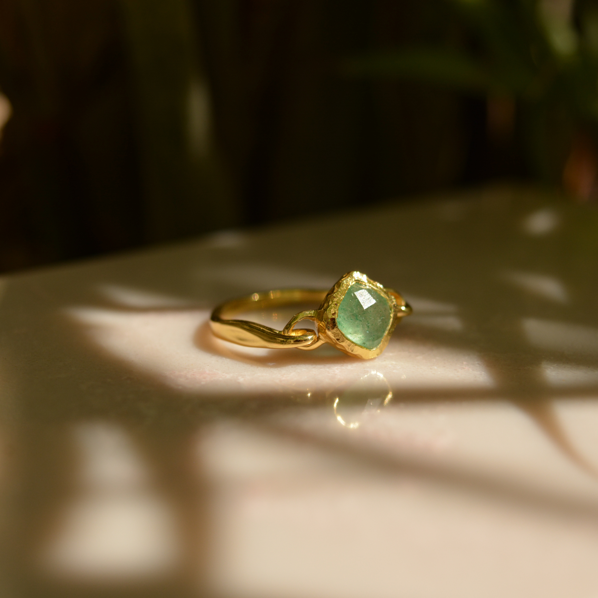 A handcrafted 18kt gold plated Calm Aura Ring featuring a square green aventurine stone, captured in warm natural sunlight with soft leaf shadows.