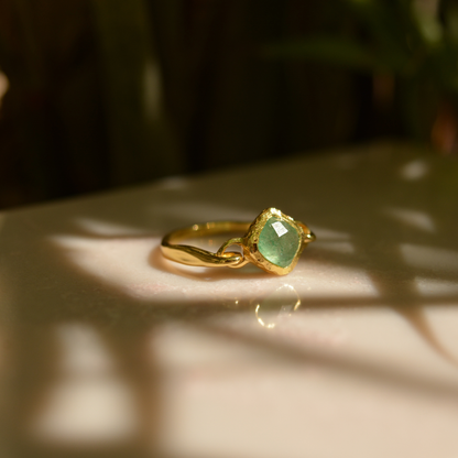 A handcrafted 18kt gold plated Calm Aura Ring featuring a square green aventurine stone, captured in warm natural sunlight with soft leaf shadows.